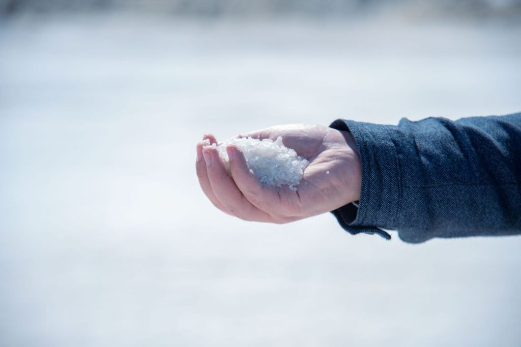 A close-up view of a hand holding white salt crystals outdoors, capturing texture and detail.